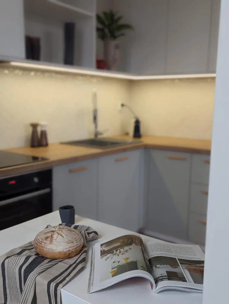 Nowoczesna kuchnia z jasnoszarymi frontami, drewnianym blatem i otwartą książką na wyspie - gotowa do zamieszkania.