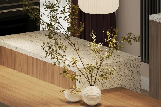 Zbliżenie na drewniany stół z ceramiczną wazą i gałązkami, przy wyspie z terrazzo i plisowanymi lampami wiszącymi.